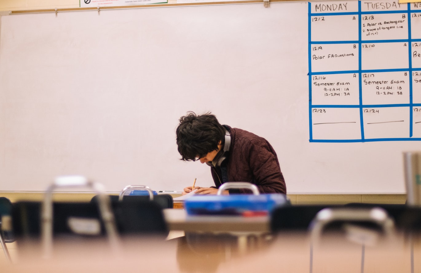 Man in a brown sweater hunched over school work.