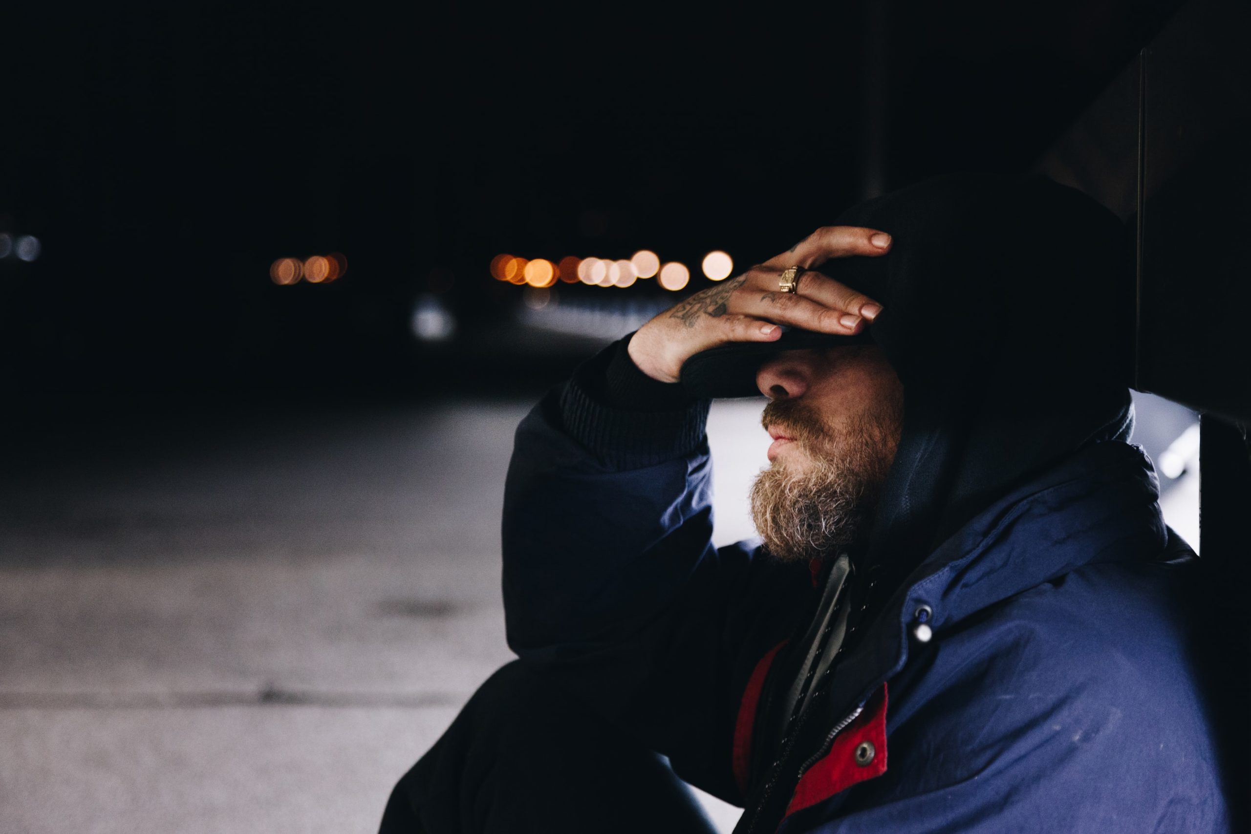 man sits with a hood over his head and a hand covering his face