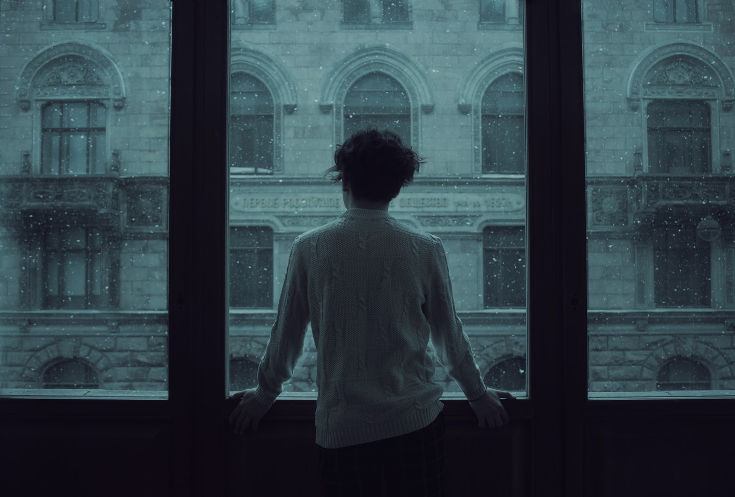 person looking out of a window to a gloomy building